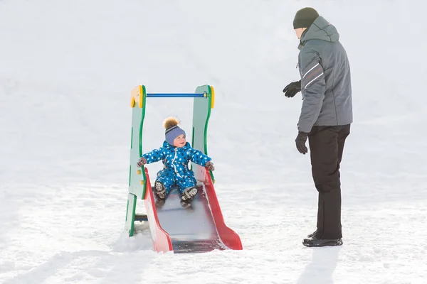 Vater geht mit seinem Sohn im Winter spazieren und rollt den Hügel hinunter — Stockfoto