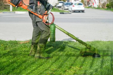 Tulum giyen adam ve yeşil çim biçme benzinli çim makası ile lastik çizmeler.