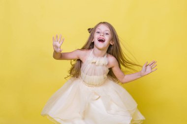 Sarı bir arka plan üzerinde elbiseli genç kız kamera için poz veriyor.