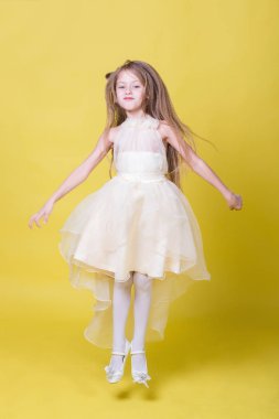 Sarı bir arka plan üzerinde elbiseli genç kız kamera için poz veriyor.