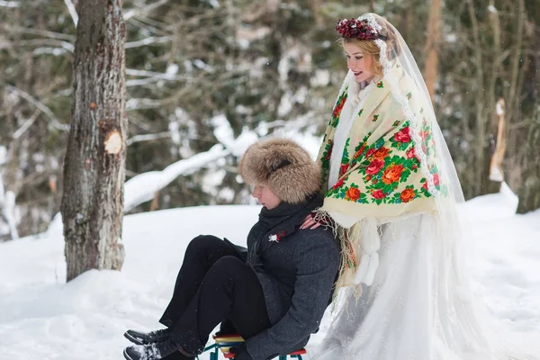 Groom and bride in the cold winter forest with the big wooden sled — Stock Photo, Image