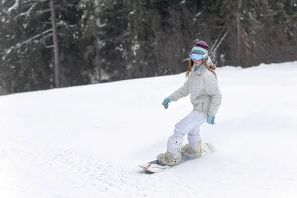 Νεαρή γυναίκα snowboarder σε κίνηση σε snowboard στα βουνά — Φωτογραφία Αρχείου