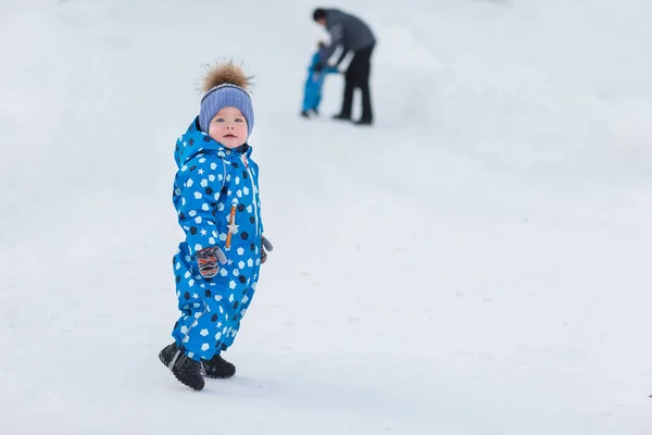 Портрет симпатичного мальчика-близнеца в зимнем парке на фоне его отца и брата — стоковое фото
