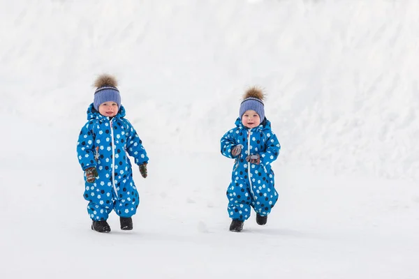 Niños gemelos caminando en el parque en el invierno en monos a juego —  Fotos de Stock