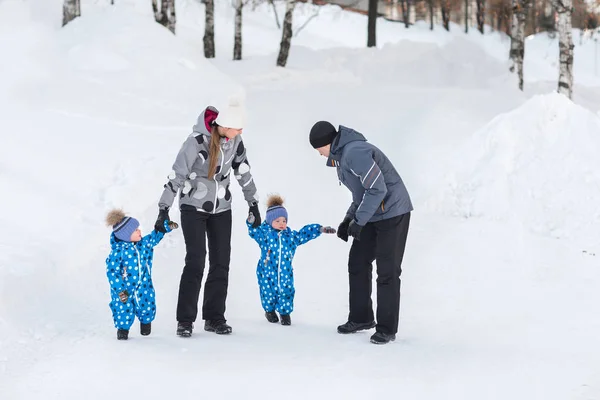 Отец, мать и дети, близнецы держатся за руки и ходят по снегу — стоковое фото