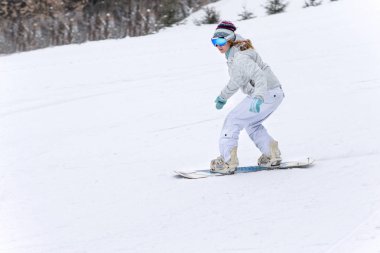 Genç kadın snowboardcu dağlarda snowboard yapıyor.