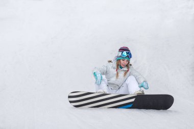 Tepenin yamacında oturan snowboard 'lu genç bir kadın.