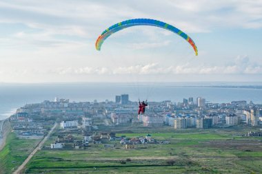 Güneşli bir günde şehrin üzerinde paraşütçüler uçuyor.