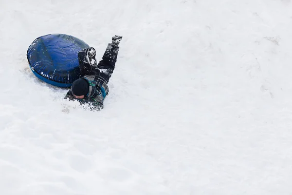 Lustiges Kind fällt im Winter mit Schläuchen aus den schneebedeckten Bergen — Stockfoto