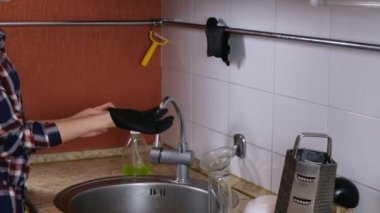 Mutfakta bir ekose gömlek, kadın kauçuk eldiven giyer ve cam lavaboya yıkar.
