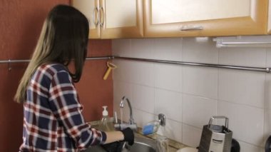 Lastik eldiven ekose gömlekli uzun saçlı esmer Cam ve fincan tabağı yıkama.
