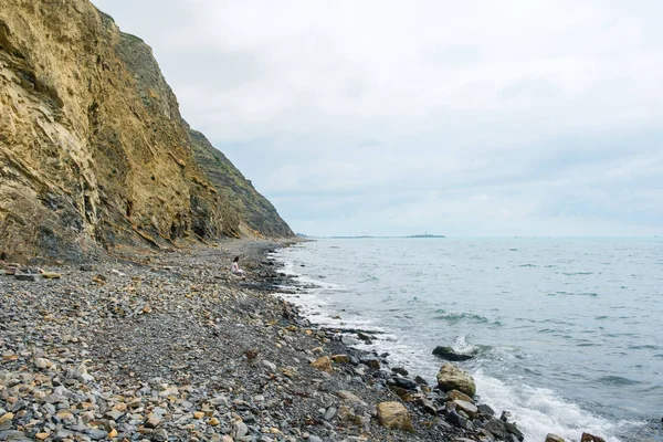 Одинокая девушка, сидящая на берегу между скалой и морем . — стоковое фото