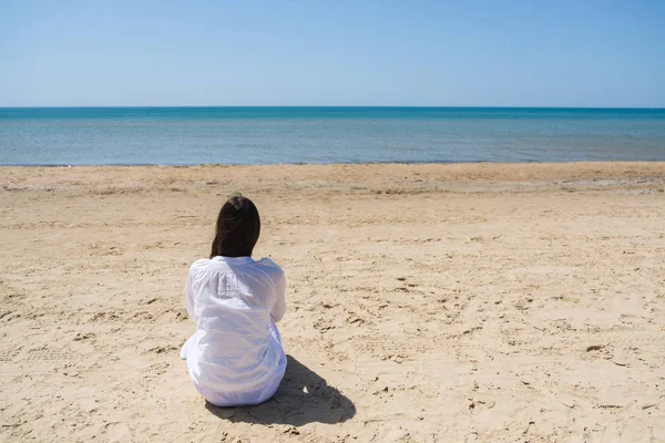 Samotna kobieta brunetka z lobg włosów na plaży i patrząc na morze. Widok z tyłu. — Zdjęcie stockowe