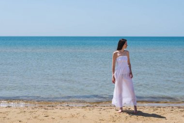 Beyaz elbiseli bir kadın kumsalda yürür