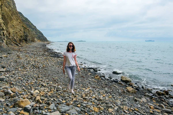 Chica joven y solitaria caminando en la orilla entre la roca y el mar . — Foto de Stock