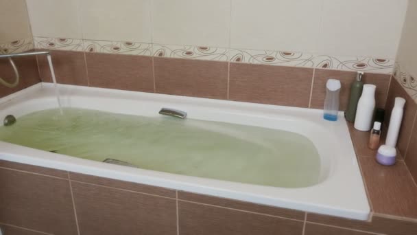 A água derrama da torneira na banheira. Uma banheira cheia de água . — Vídeo de Stock