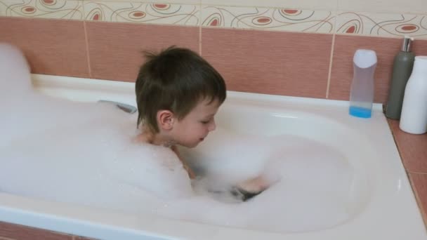 Pojke 6-7 spelar med vitt skum i badkaret. Tar skum och sätter på huvudet. — Stockvideo
