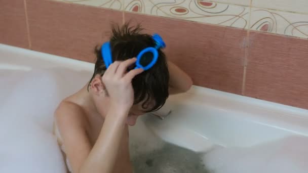 Kluk 6-7 let sedí v bublinkové lázni a snaží se nosit brýle. — Stock video