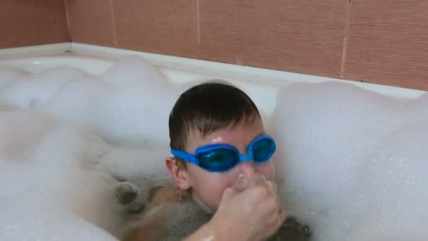 Chłopiec 6-7 lat nurkuje w płyn do kąpieli, spójrz na aparat i się śmieje. — Wideo stockowe
