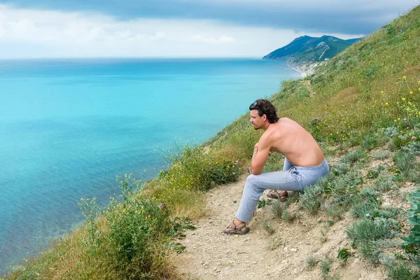 Handsome man sitting on hill and looking on sea. Side view.
