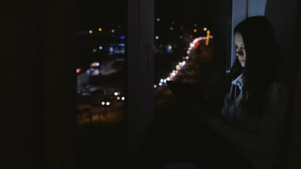 Mulher navegando na web no computador tablet sentado no peitoril da janela na noite escura. Fundo rodoviário . — Vídeo de Stock