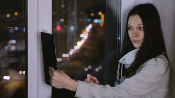 Nő ül az ablakpárkányon, a sötét éjszakában, és ezzel selfies a tabletta. — Stock videók