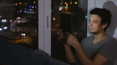 Adam tablete sohbet ve gülüyor. Pencere içinde belgili tanımlık karanlık geceleri oturup....