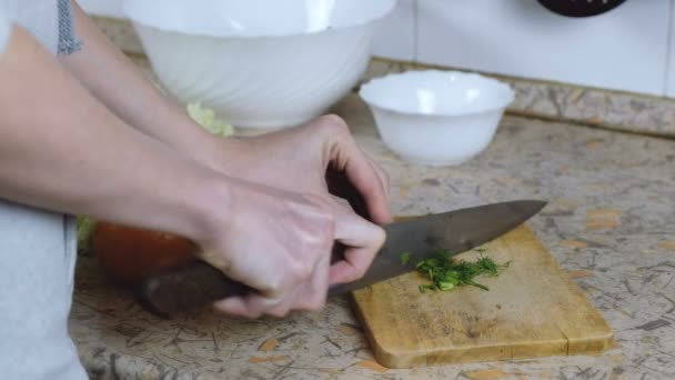 Unrecognizable woman cuts dill on a cutting board on a kitchen table. Hands close up. — Stock Video