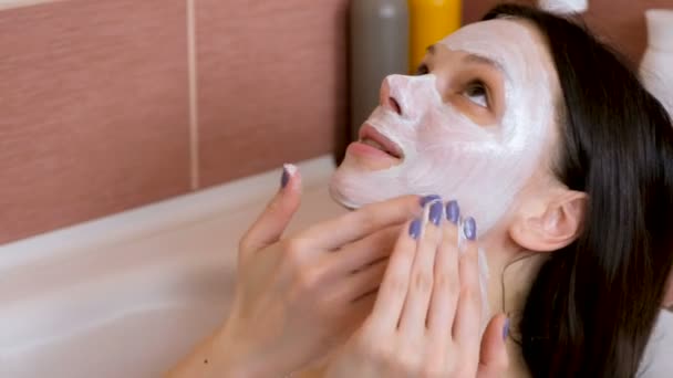 Schöne brünette Frau legte blaue Lehmmaske auf ihr Gesicht im Badezimmer. Wellness zu Hause. Gesicht aus nächster Nähe — Stockvideo