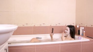 Banyo ve genel görünüm cep telefonuyla chattin yüzünde maske olan esmer kadın yatıyor