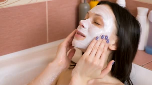 Mooie brunette vrouw zet blauwe klei masker op haar gezicht in de badkamer. Slomo. Close-up gezicht — Stockvideo