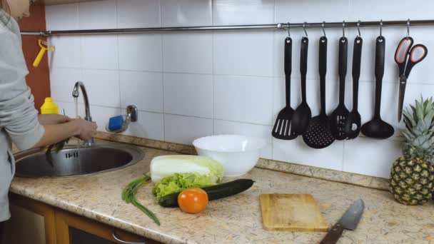 Woman brunette washes vegetables onion, dill, tomato for salad in the kitchen. Side view. — Stock Video