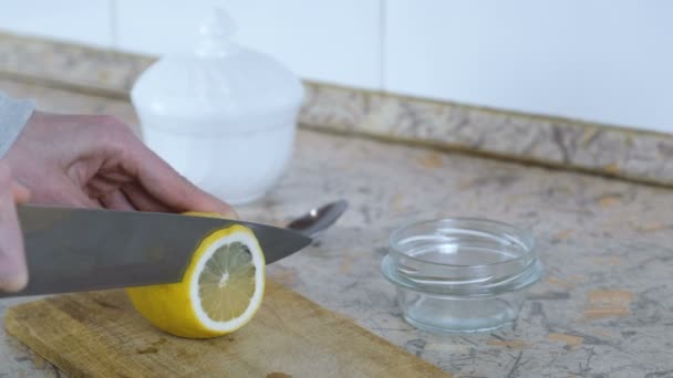 Gros plan d'une femme coupant du citron à la main sur une planche à découper en bois dans la cuisine . — Video