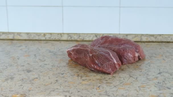 Dos grandes trozos jugosos de carne en una mesa de cocina. Vista lateral. Movimiento de cámara de izquierda a derecha . — Vídeos de Stock