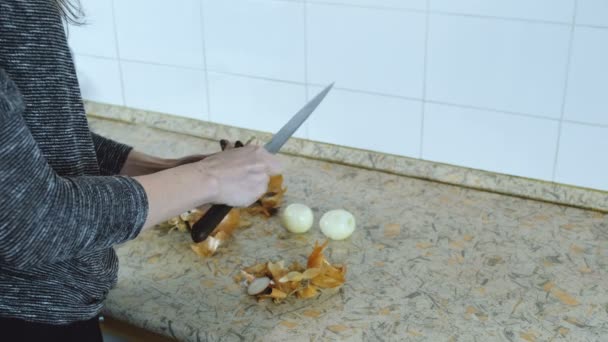 Las manos de mujer de cerca limpian una cebolla de la cáscara de la mesa de la cocina. Vista lateral . — Vídeos de Stock