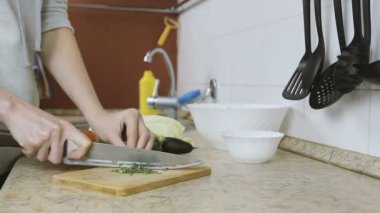 Tanınmayan kadın mutfakta bir kesme tahtası dereotu keser. Eller yakın çekim