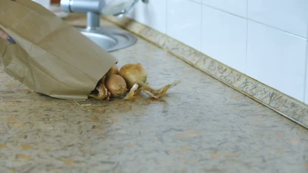 Κρεμμύδι χύνεται από μια χάρτινη σακούλα στο τραπέζι της κουζίνας. Αργή κίνηση. — Αρχείο Βίντεο