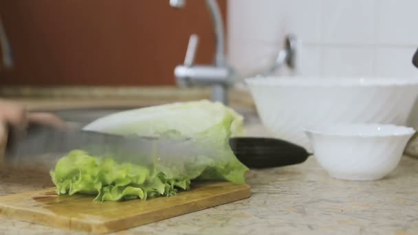 Крупним планом жіночі руки вирізають салат на обробній дошці в кухонному столі. Ніж для ножів . — стокове відео