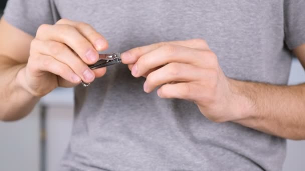 El hombre se corta las uñas con Clippers. De cerca las manos. Camiseta gris en el fondo . — Vídeos de Stock