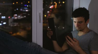 Adam tablet ve cep telefonu arıyor. Pencere karanlıkta oturup....