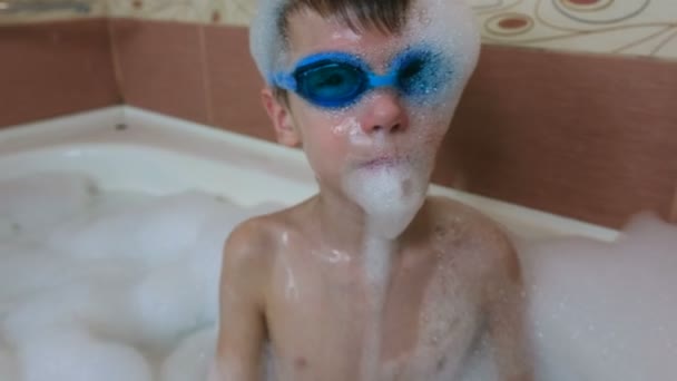 Garçon 6-7 ans dans la mousse et des lunettes pour nager assis dans la salle de bain. Gros plan sur le visage . — Video