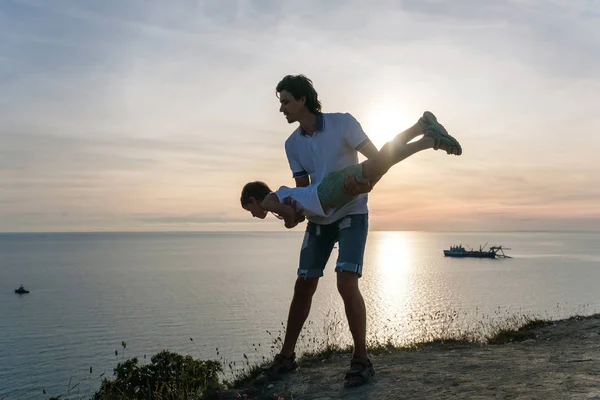 Syn na tatusiowie ręce na górze z widokiem na nabrzeże. Gra ze sobą, o zachodzie słońca. Zabawne rozrywką. — Zdjęcie stockowe
