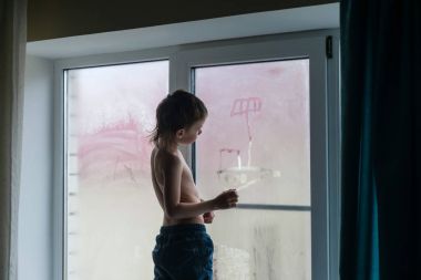 Altı yaşında çocuk kot giyen bir sisli pencere ayakta bir teknede kenarında çizer..