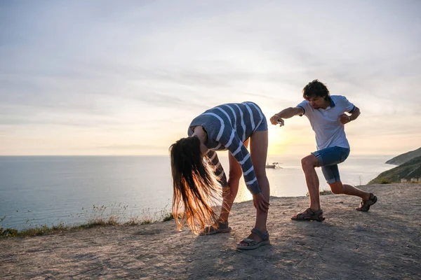 Mann und Frau amüsieren sich auf dem Berg mit Meerblick und nehmen lustige Posen ein. Sonnenuntergang am Abend — Stockfoto