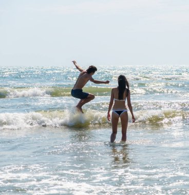 Denizin dalgaları aracılığıyla adam atlar. Kadın değer yakındır ve ona bakar.