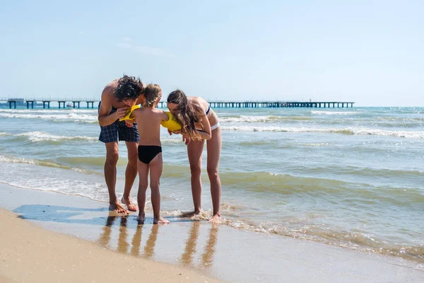 両親は、浜の息子のため黄色の水の翼を膨らませます。家族での休暇. — ストック写真