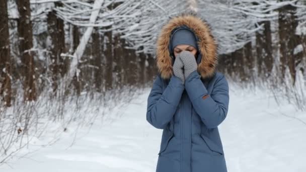 Woman warms her hands in the cold with her breath in the winter forest. — Stock Video