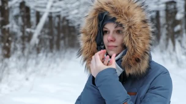 Mujer con chaqueta calienta sus manos desnudas en el frío con su aliento en el bosque de invierno. Vista lateral . — Vídeo de stock
