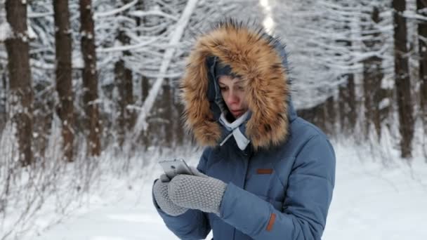 Donna in abiti caldi nel parco invernale toglie il morsetto per utilizzare un telefono cellulare . — Video Stock