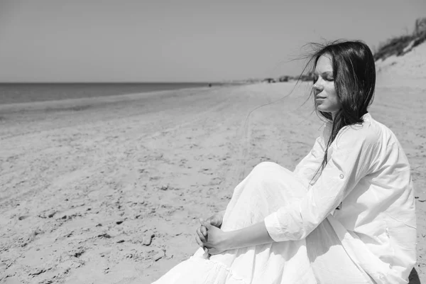 Mujer joven mirando hacia otro lado mientras está sentada en la orilla del mar — Foto de Stock